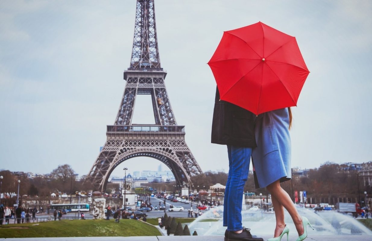 Enamorados tras un paraguas rojos en frente de la Torre Eiffel